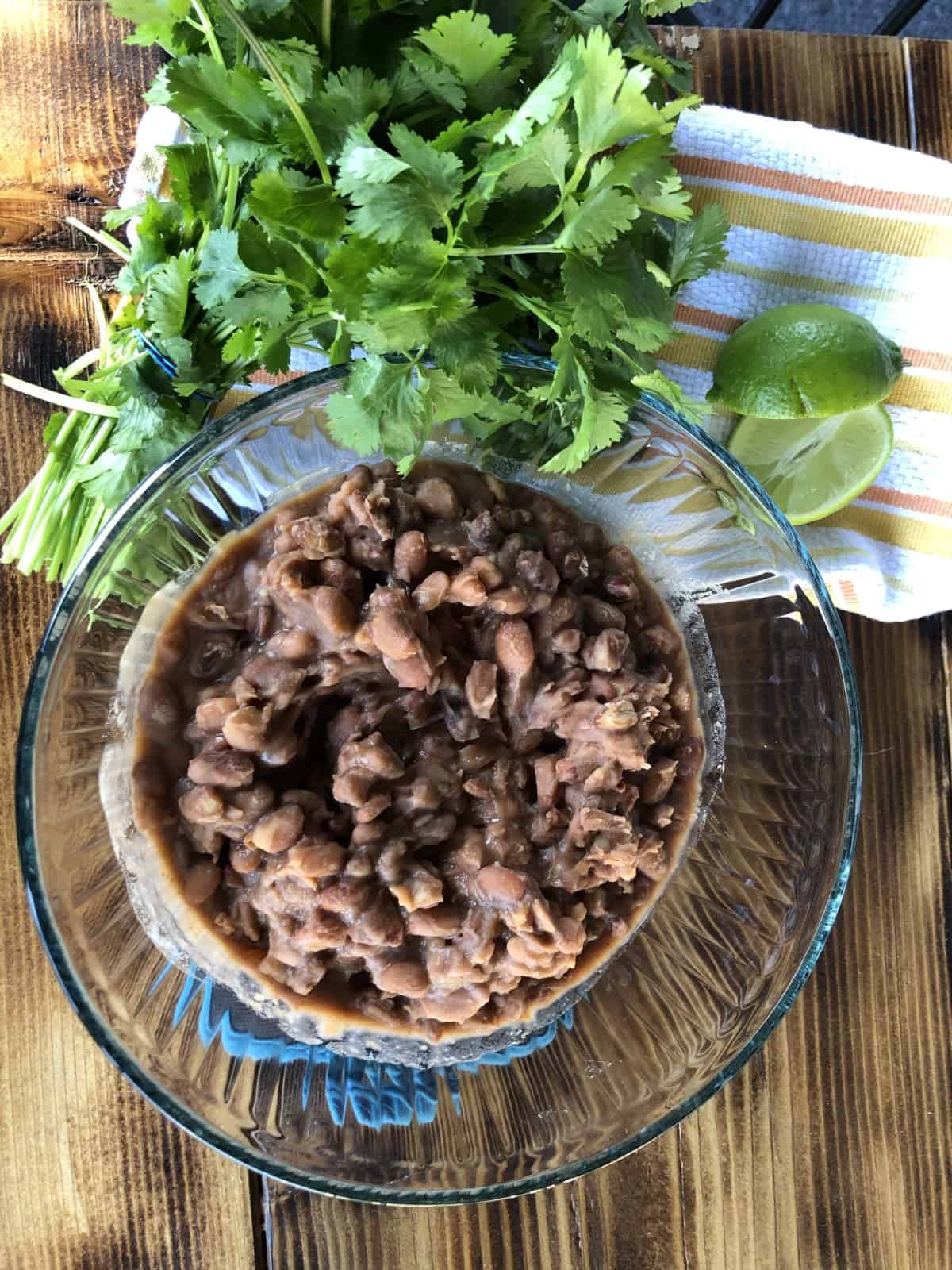 Cooked pinto beans in glass bowl with fresh cilantro and lime on wooden table