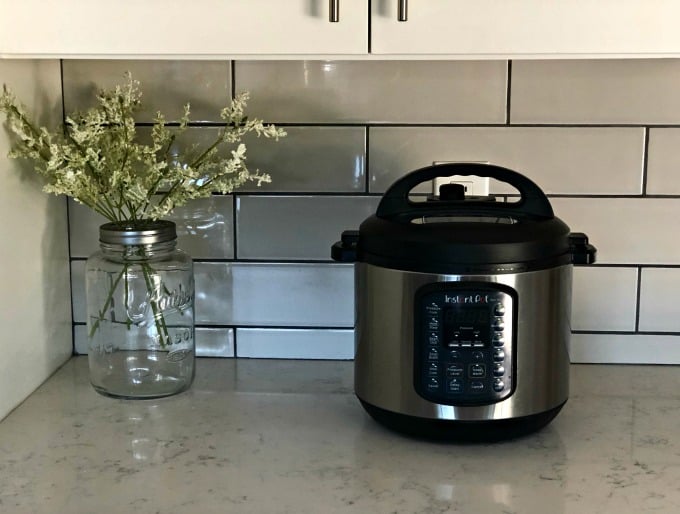 InstantPot on kitchen counter near jar with flowers.