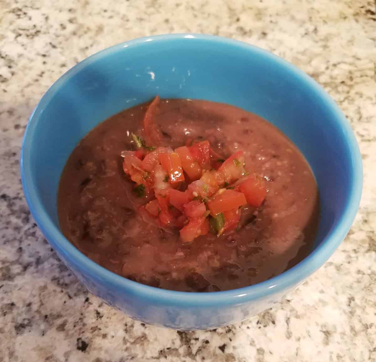 Instant Pot black bean soup topped with pico de gallo in blue bowl.