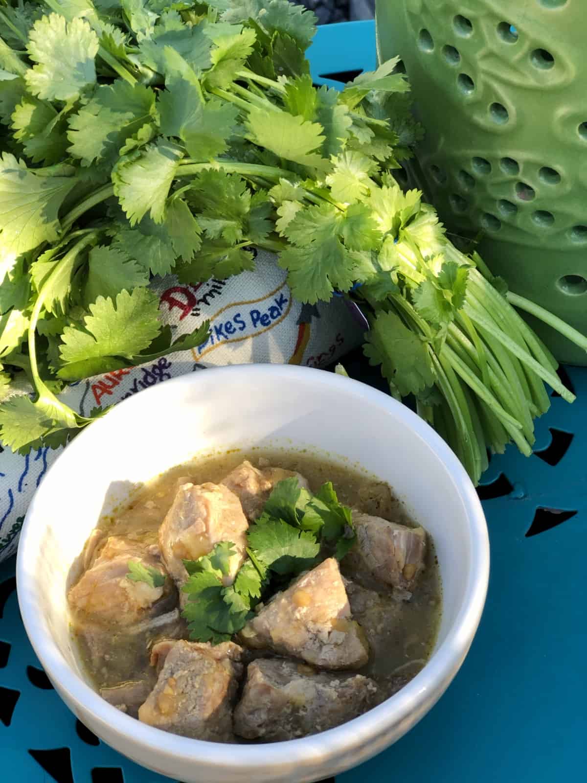 Bowl of pork chili verde on blue table with bunch of fresh cilantro