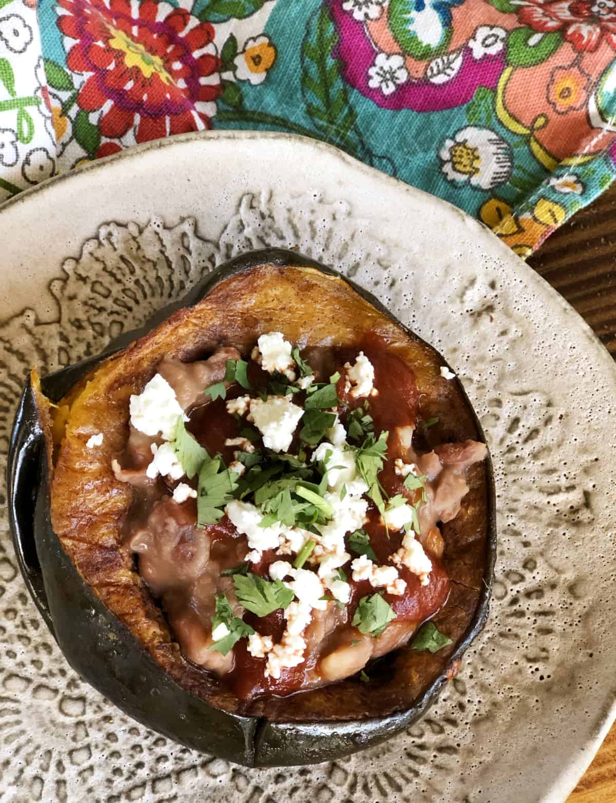 Roasted acorn squash with pintos, red chili sauce, crumbled cheese and cilantro on pottery plate.