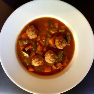 wide rimmed shallow white soup bowl filled with vegetable meatball soup shot from above