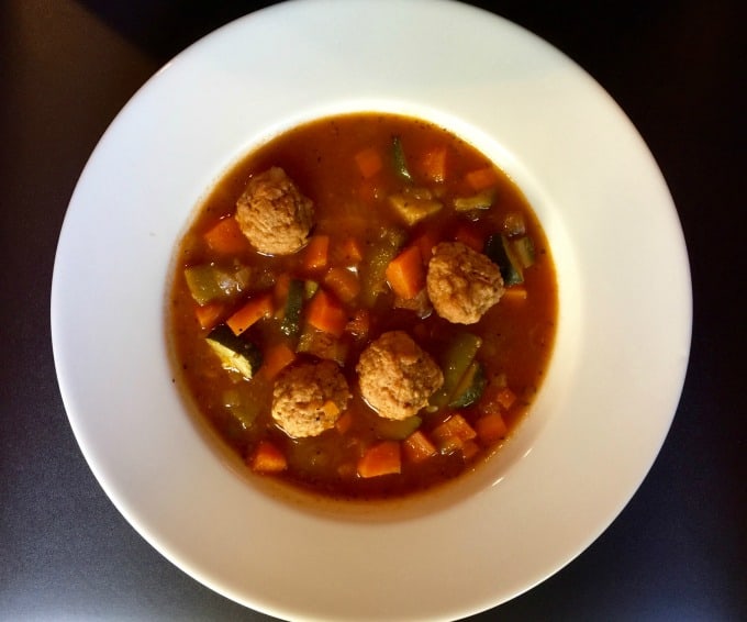 Wide rimmed shallow white soup bowl filled with vegetable meatball soup.
