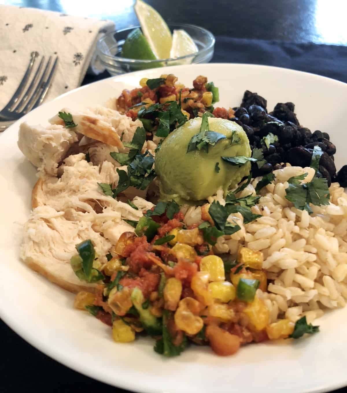 Chopped chicken, black beans, brown rice, corn salsa, guacamole and cilantro in white bowl.