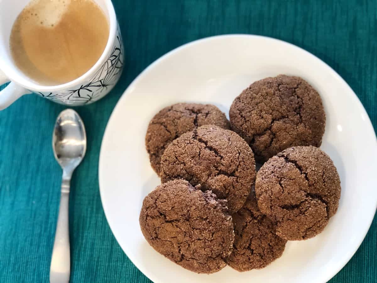 Chocolate cake mix cookies on white plate with cup of coffee and spoon.