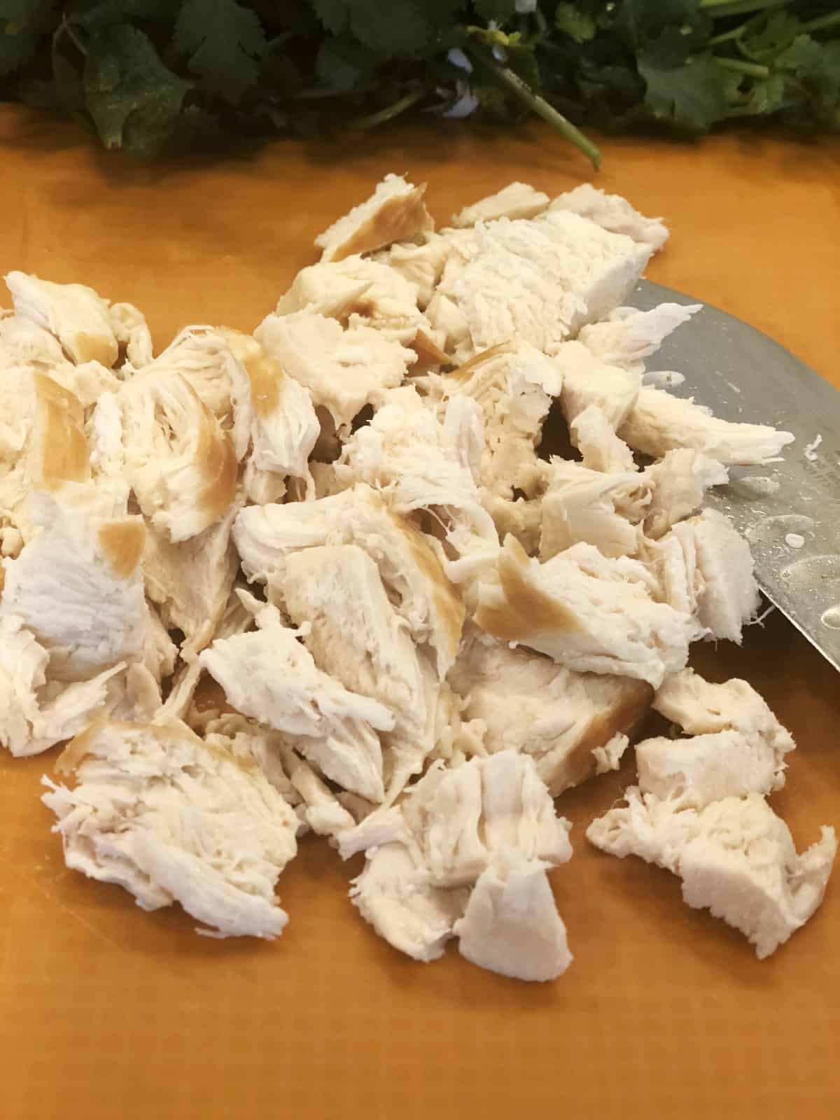 Chopped cooked chicken breast on orange cutting mat with knife.