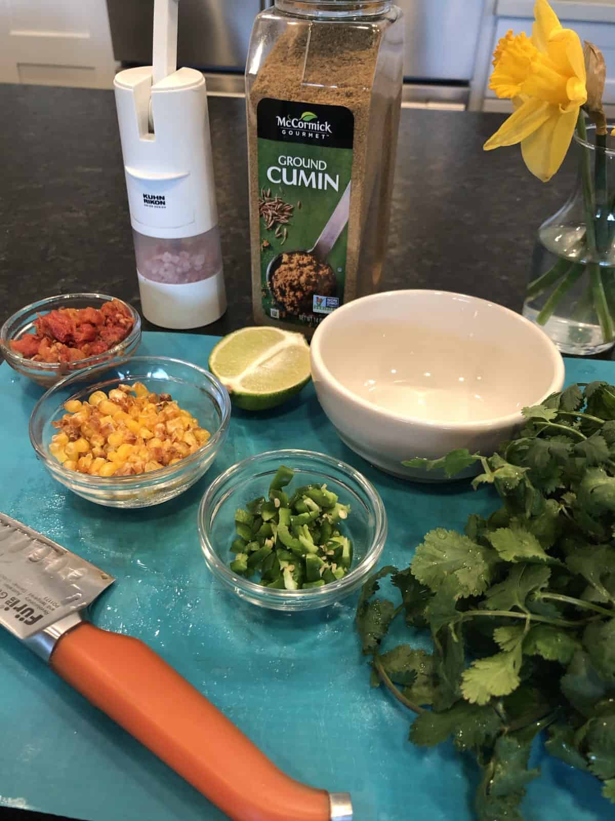 Chopped jalapeno, corn, tomatoes, lime, cumin and cilantro on cutting mat for making black bean bowls.