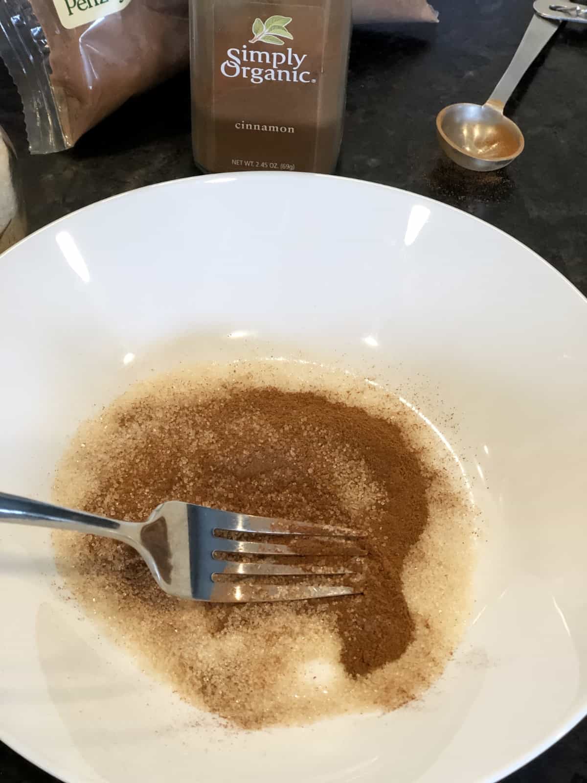 Mixing cinnamon and sugar in shallow white bowl with a fork.
