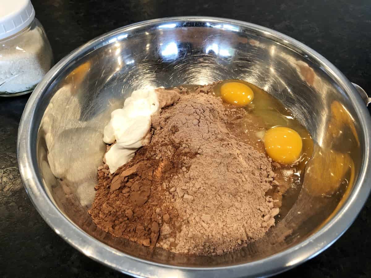 Cake mix, cocoa, sour cream, sugar and eggs in stainless steel mixing bowl.