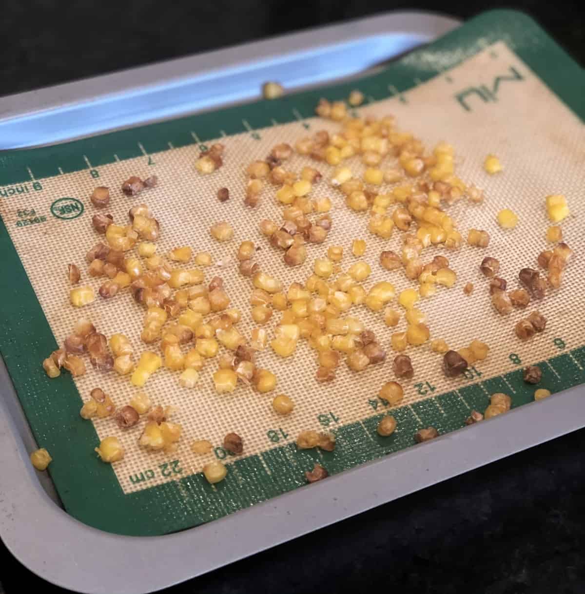 Roasted corn kernels on silat lined baking sheet.