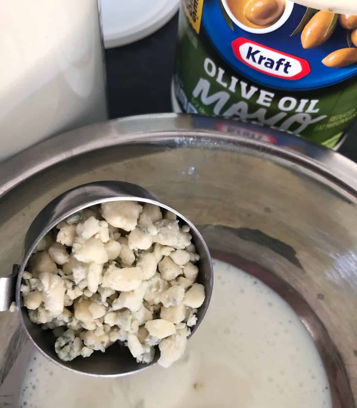 Adding crumbled blue cheese to homemade dressing in mixing bowl.