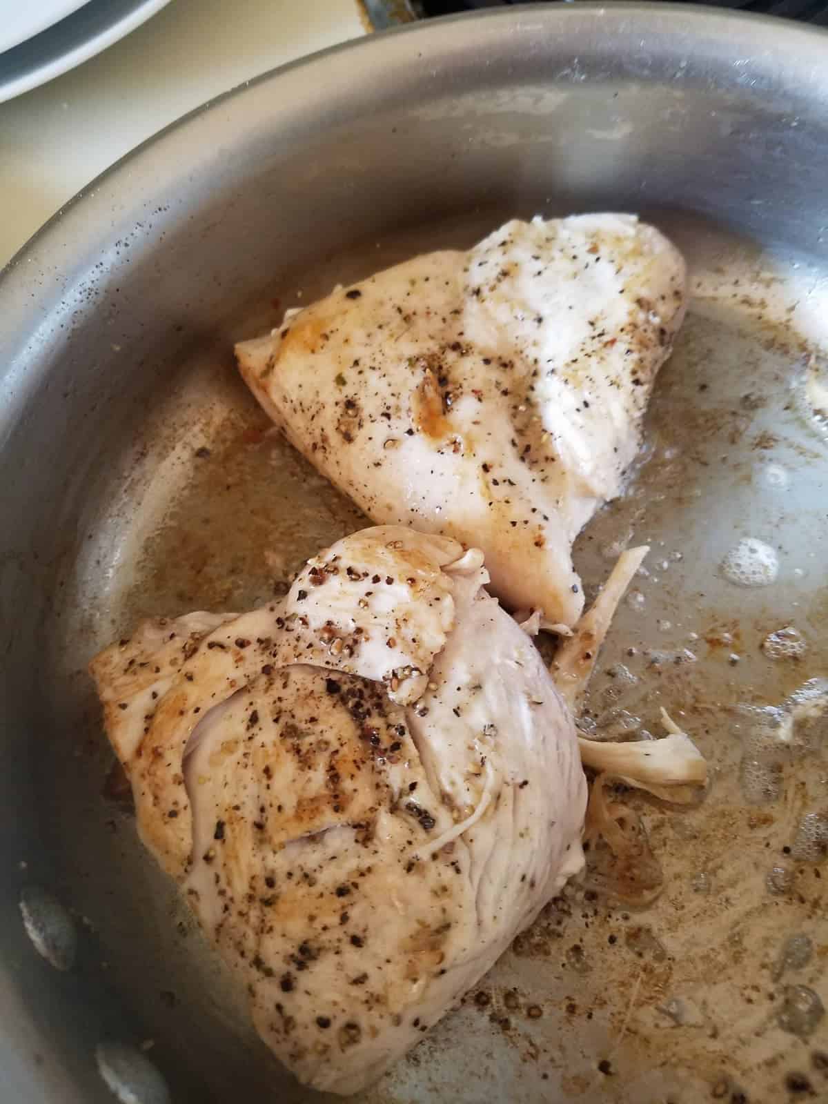 Browning two chicken breasts in saute pan on stovetop.