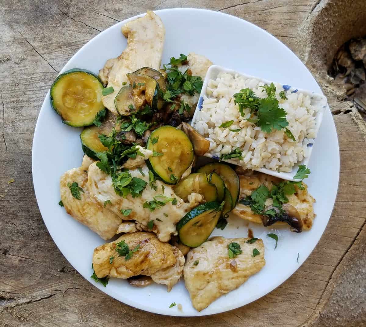 Chicken mushroom stir-fry with zucchini and side of rice on white dinner plate.