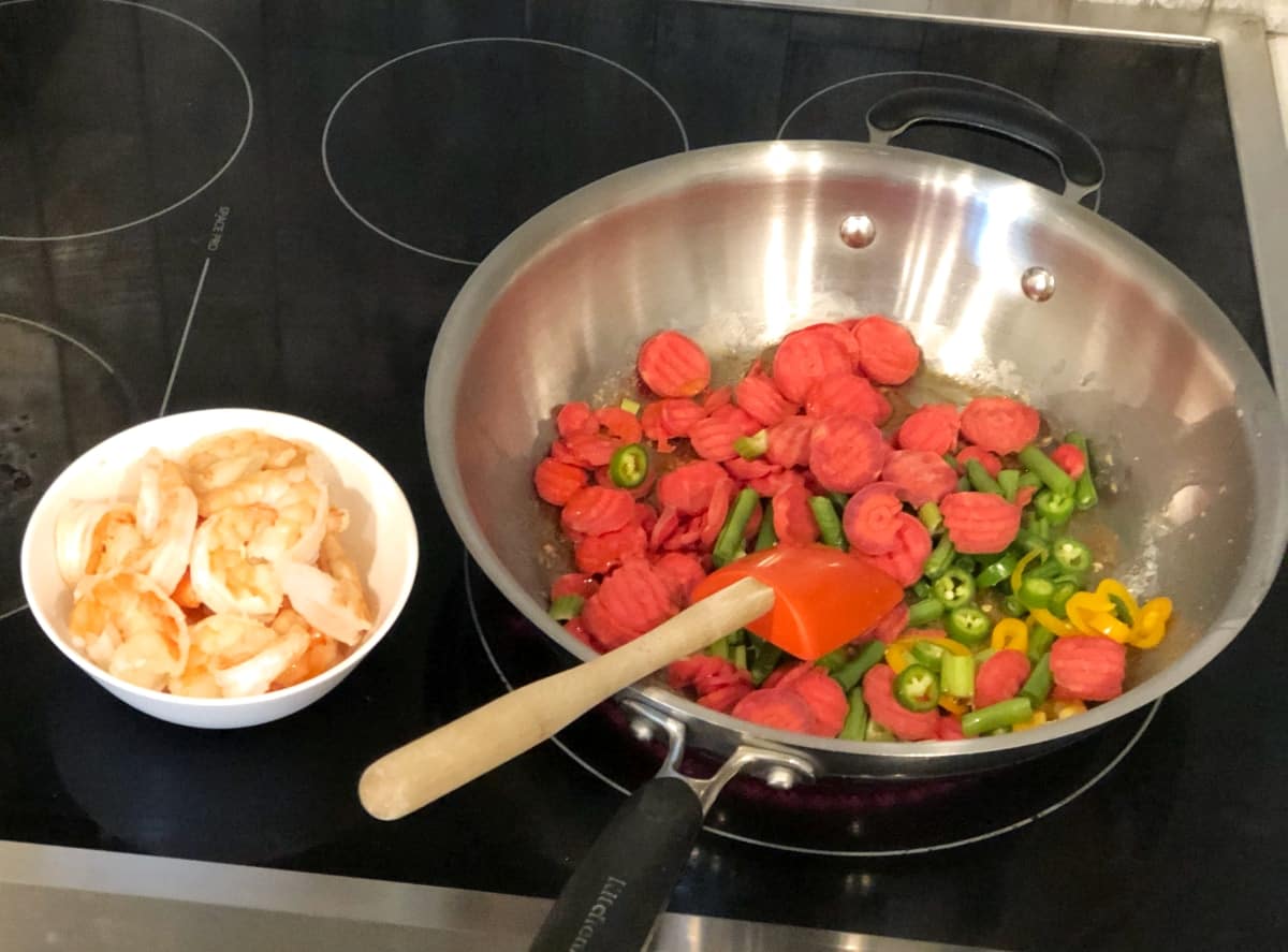 Cooking stir fry vegetables in wok with small bowl of cooked shrimp near by.
