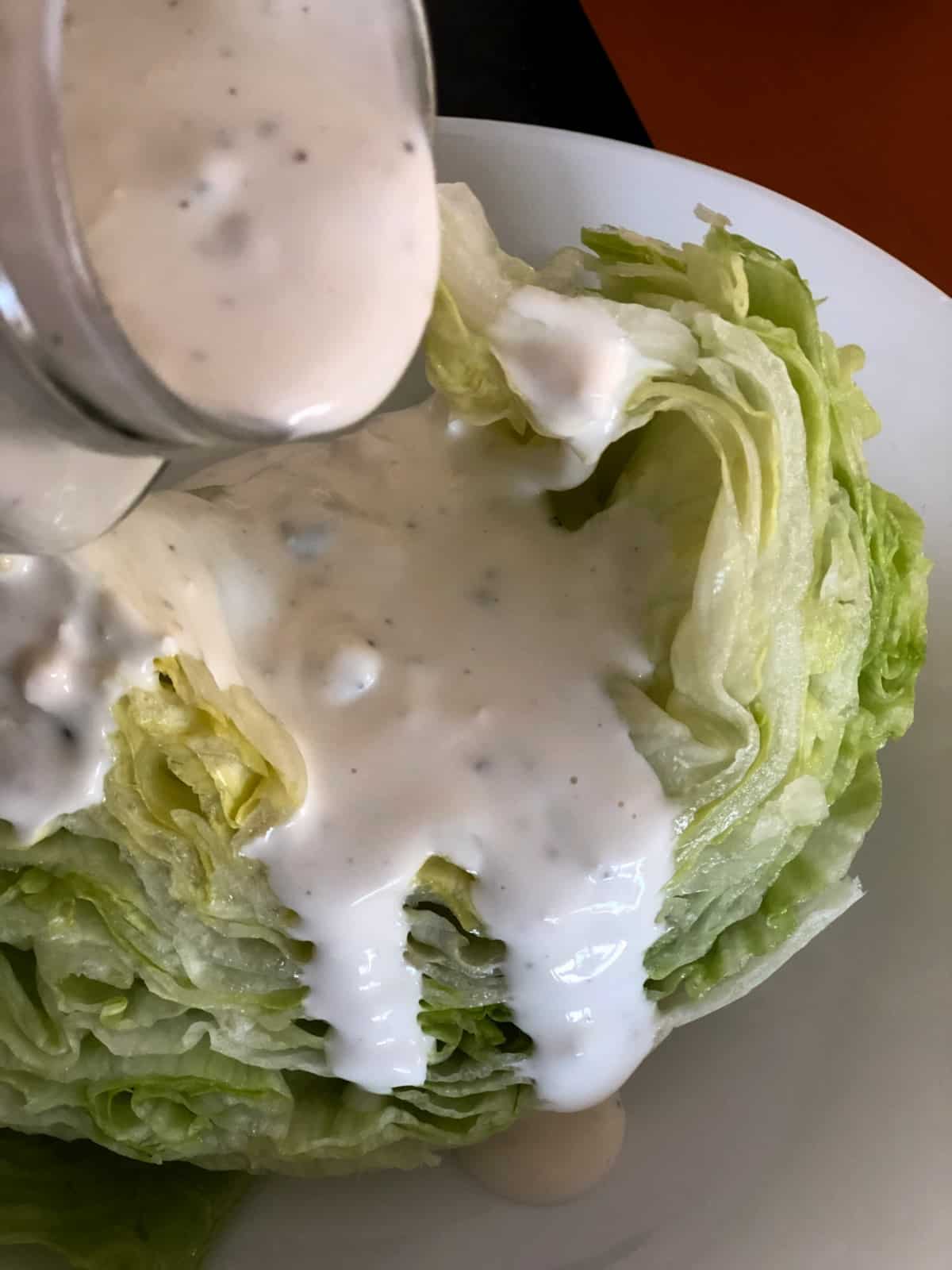 Pouring blue cheese dressing over wedge of iceberg lettuce.