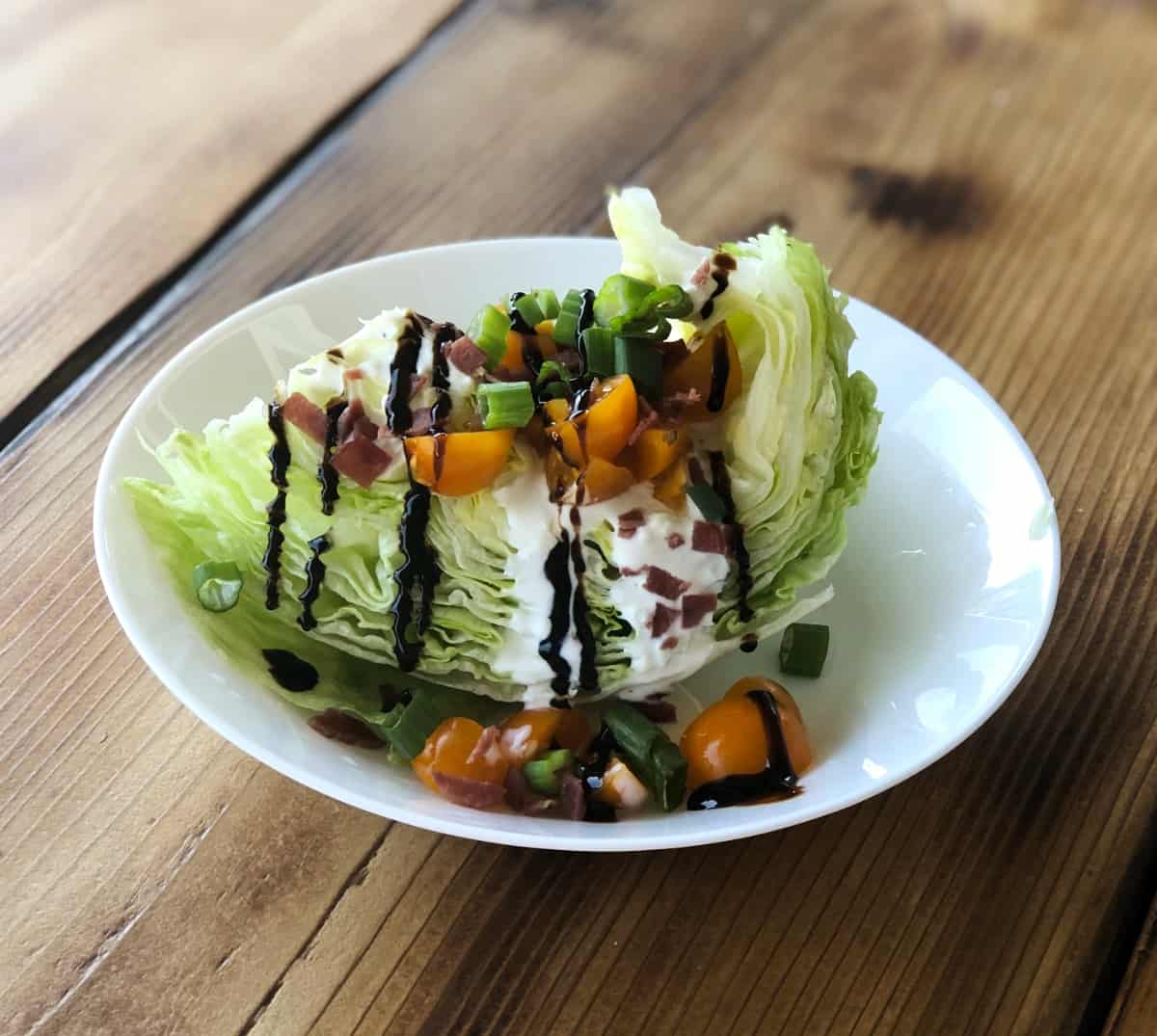 Iceberg lettuce wedge salad topped with creamy blue cheese, tomatoes, green onions, bacon bits and balsamic glaze