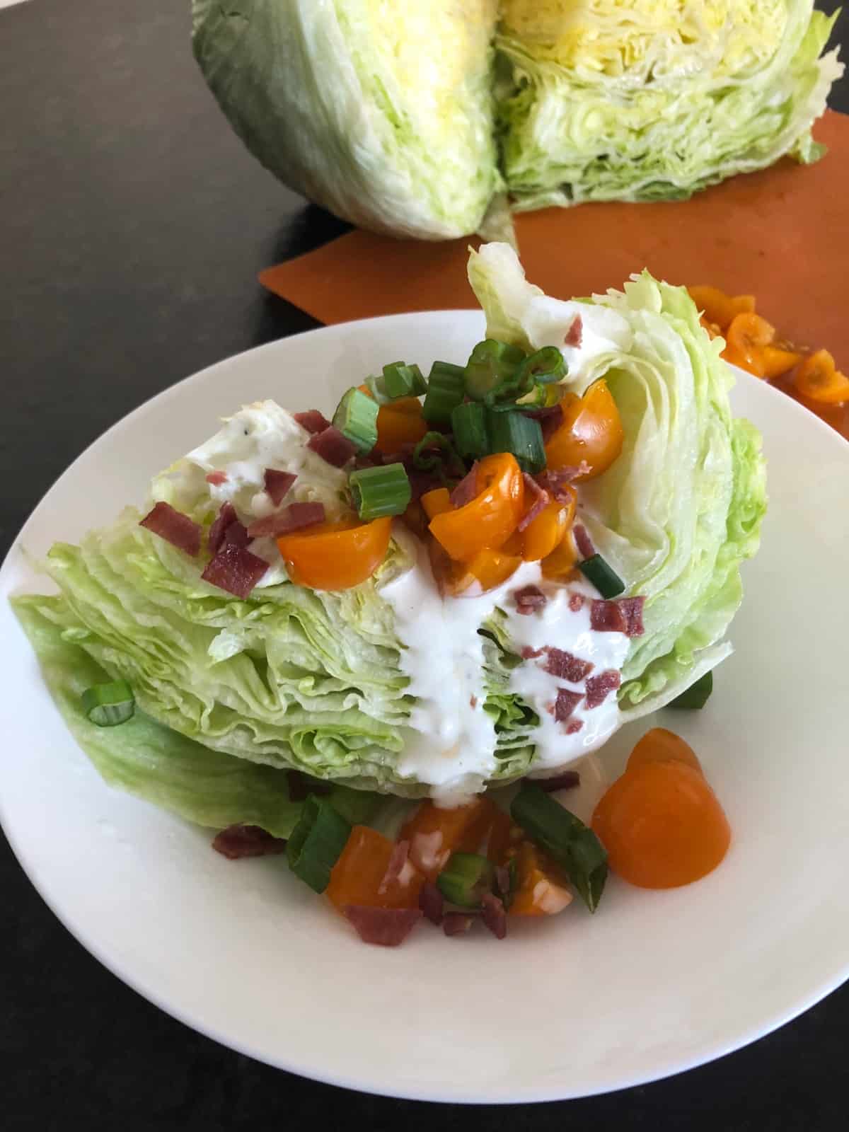 Iceberg lettuce wedge drizzled with blue cheese dressing, topped with chopped tomatoes, bacon bits and green onion