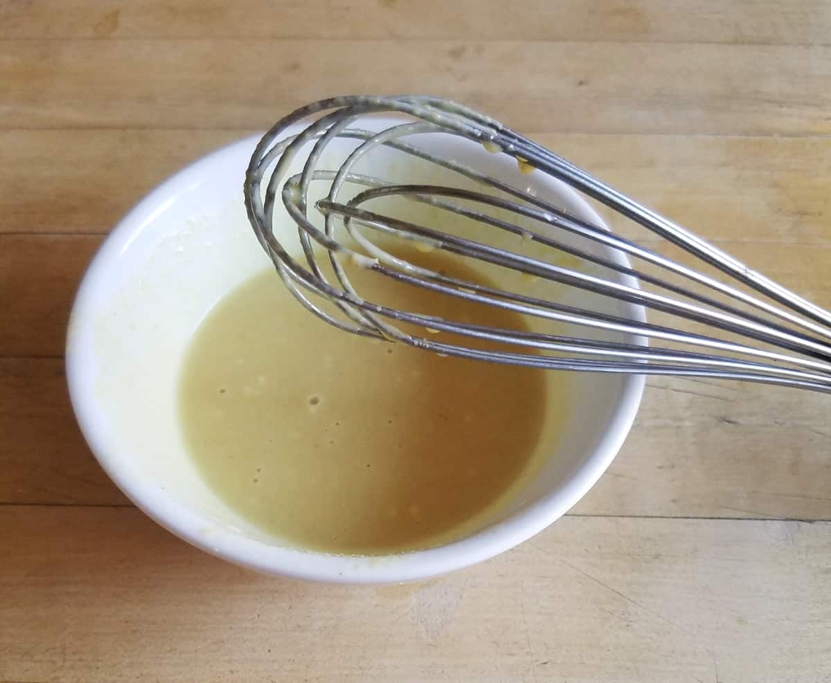 Whisking mustard, mayonnaise, honey and vinegar in small white bowl.