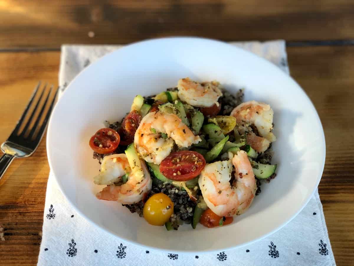 Spicy shrimp and quinoa bowl with zucchini and tomatoes in white bowl with fork.