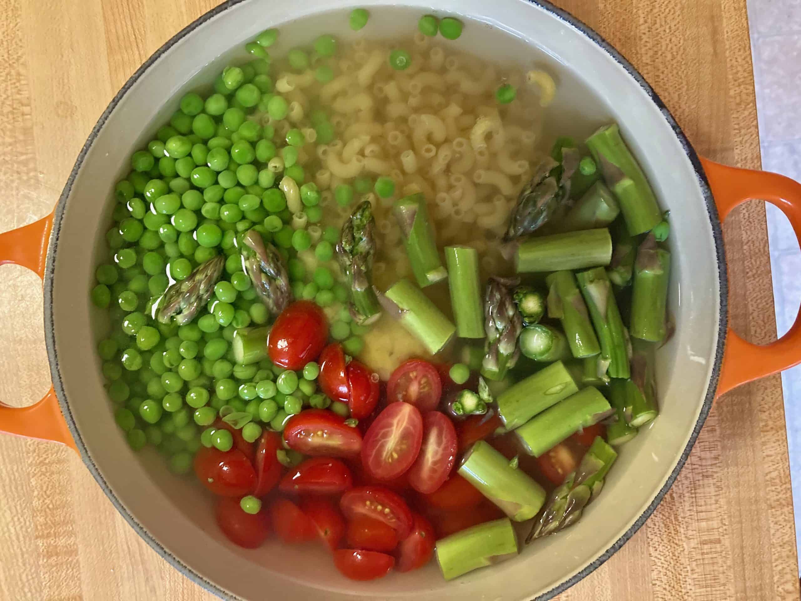 water, peas, elbow macaroni, sliced ​​cherry tomatoes and bouillon paste in a soup pot to boil, overhead shot