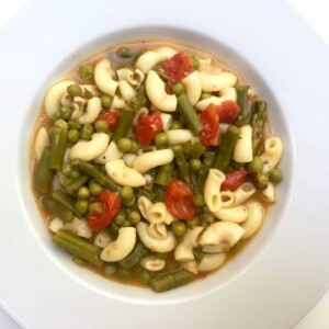 white wide rimmed shallow bowl filled with asparagus minestrone soup shot from above