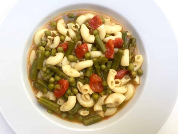white wide rimmed shallow bowl filled with asparagus minestrone soup shot from above