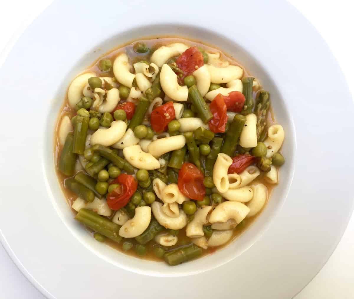 shallow white rimmed bowl filled with asparagus minestrone soup, shot from above