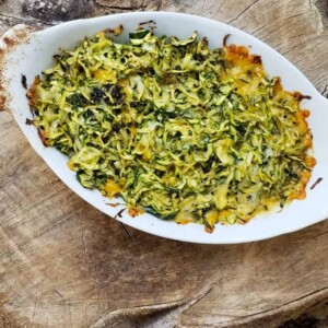 Baked cheesy zucchini gratin in baking dish sitting on wooden tree stump.
