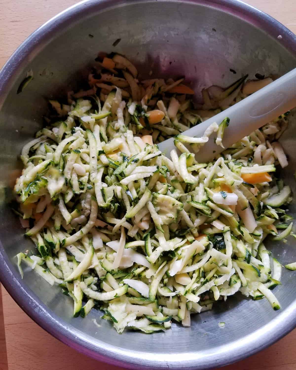 Stirring together shredded zucchini and cheese in mixing bowl.