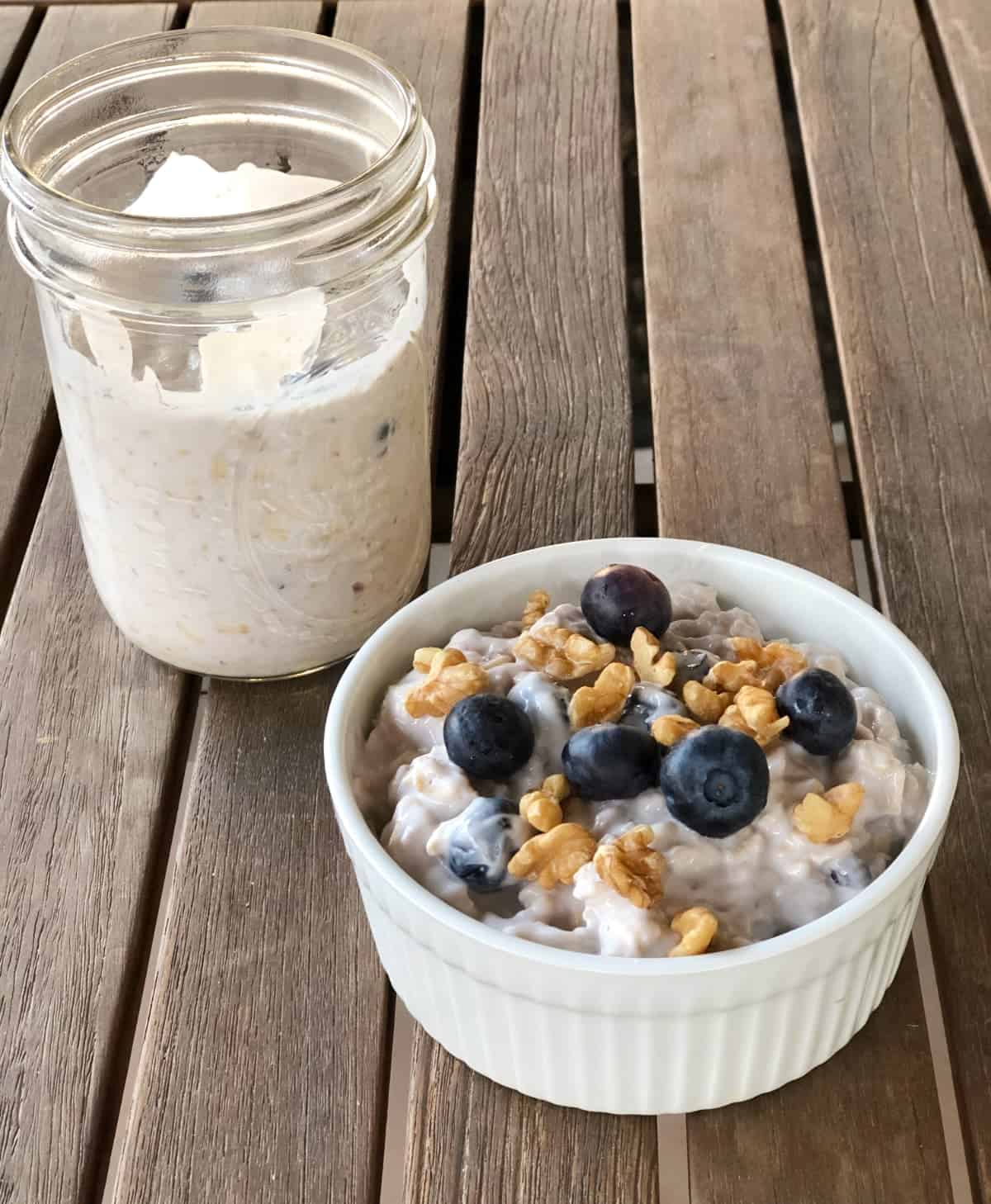 Two serving blueberry maple overnight oats, one in glass mason jar, the other topped with walnuts and fresh blueberries in small white ramekin.