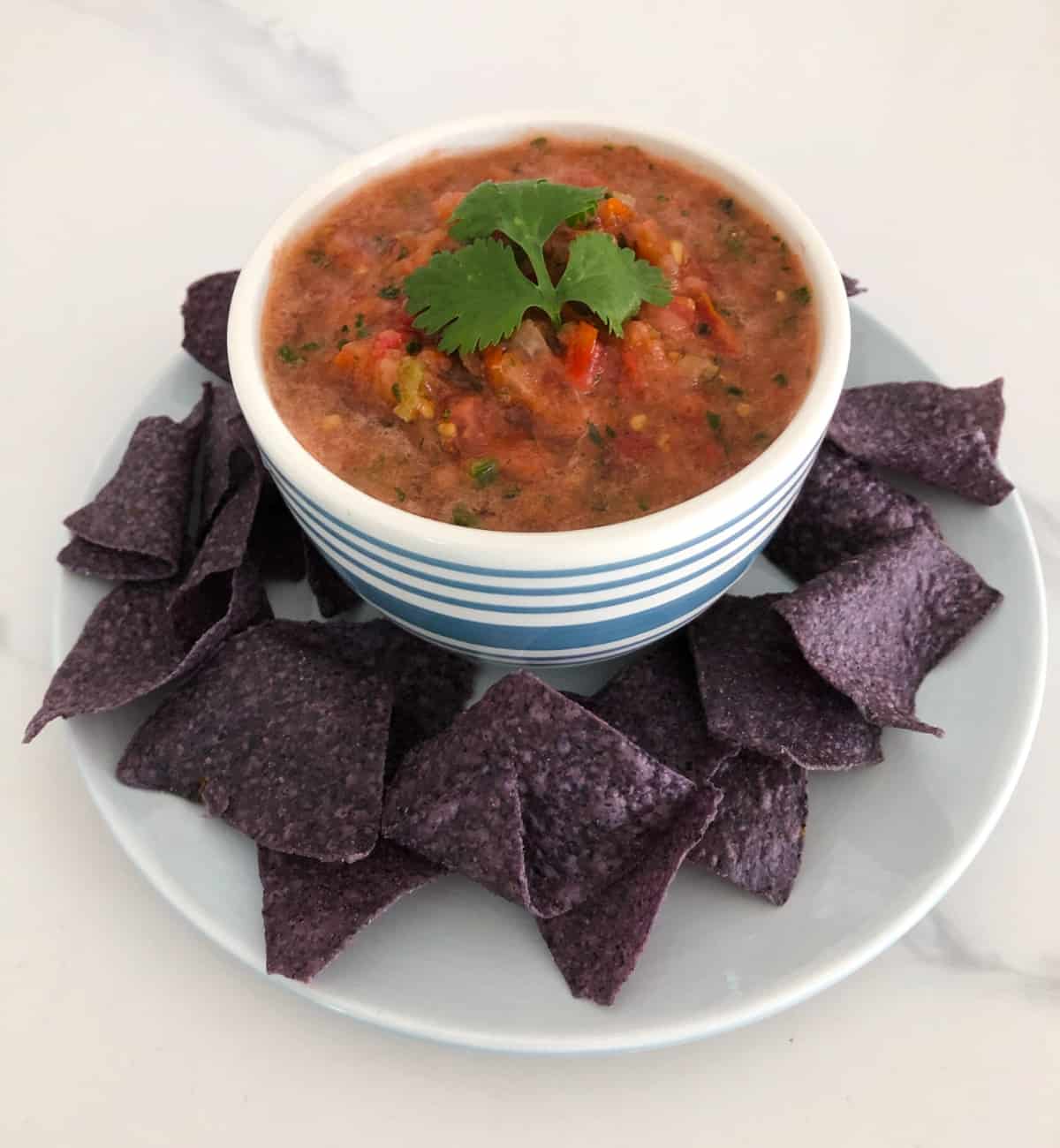 California fresh salsa in white and blue striped bowl with blue corn chips.