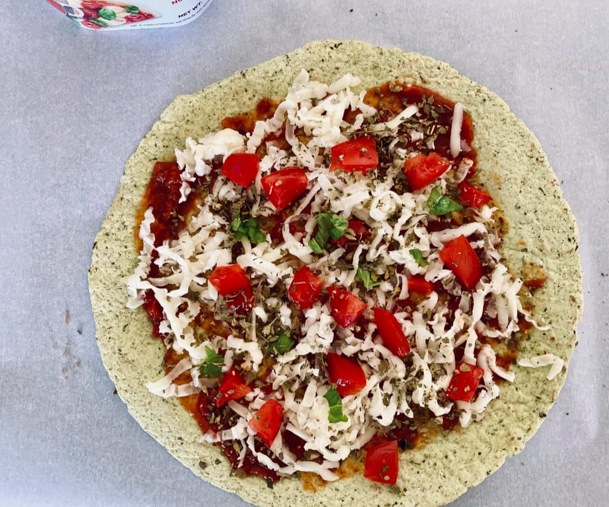 Crispy tortilla topped with pizza sauce, shredded mozzarella, chopped tomatoes and basil before baking.