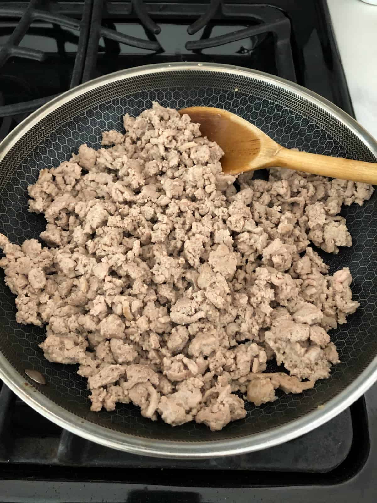 Cooking lean ground turkey in stainless pan with wooden spoon.