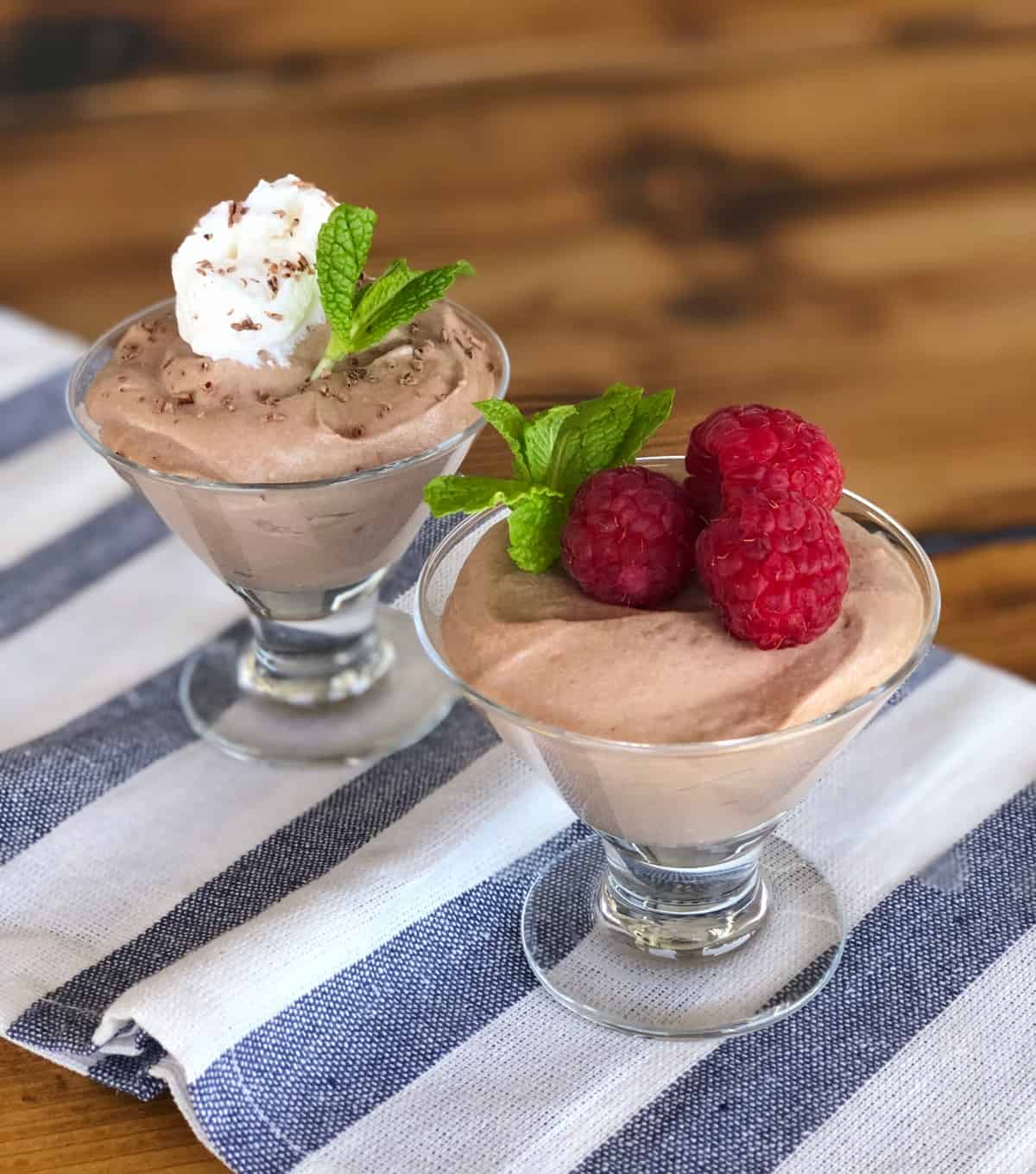 Two dessert glasses with Nutella mousse - one topped with fresh raspberries and mint, the other topped with whipped cream, chocolate shavings and mint.