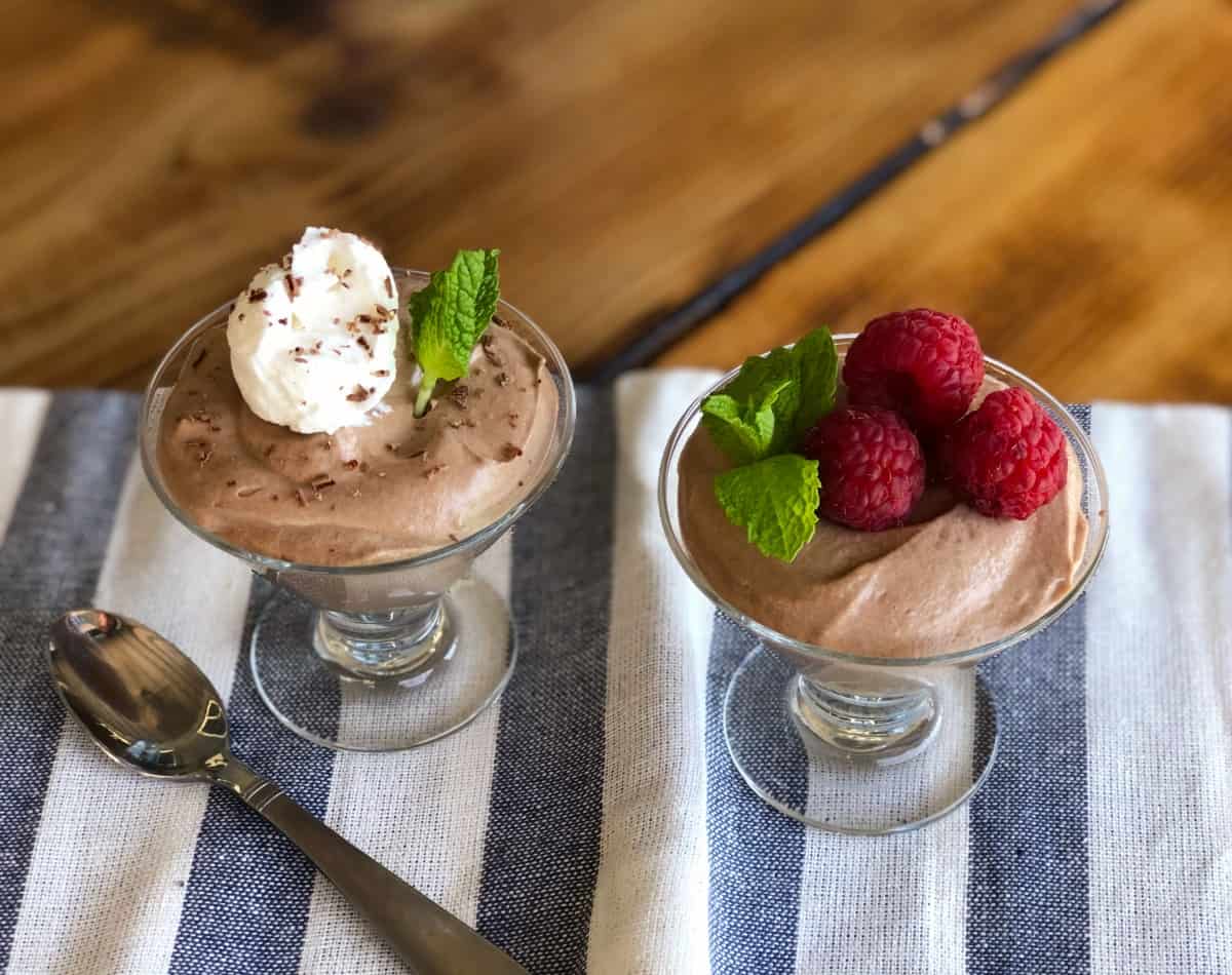 Two stemmed dessert glasses with Nutella mousse - one is topped with whipped cream and mint, the other fresh raspberries and mint.