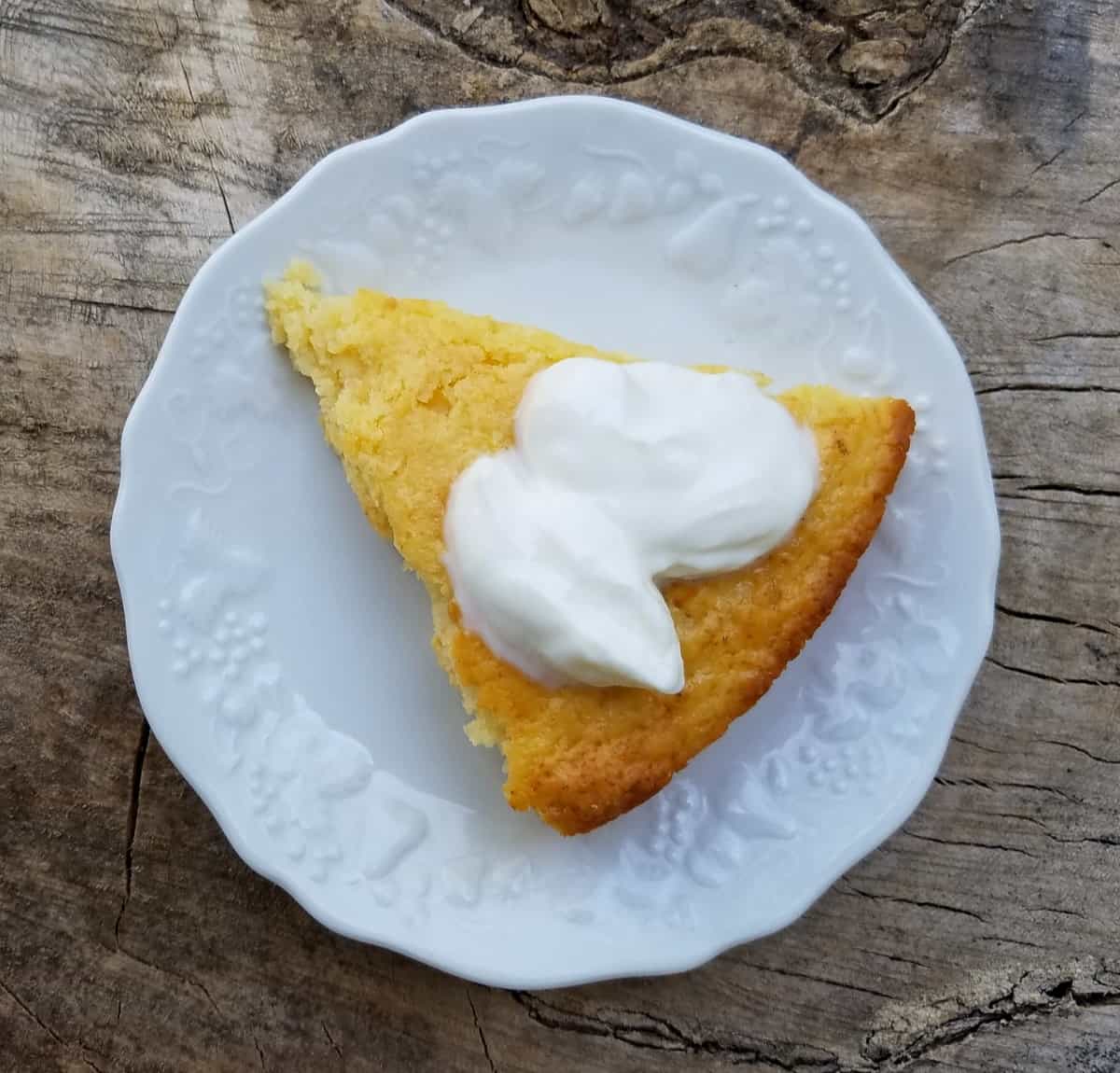 Piece of pineapple yogurt cake topped with whipped cream on small white plate.