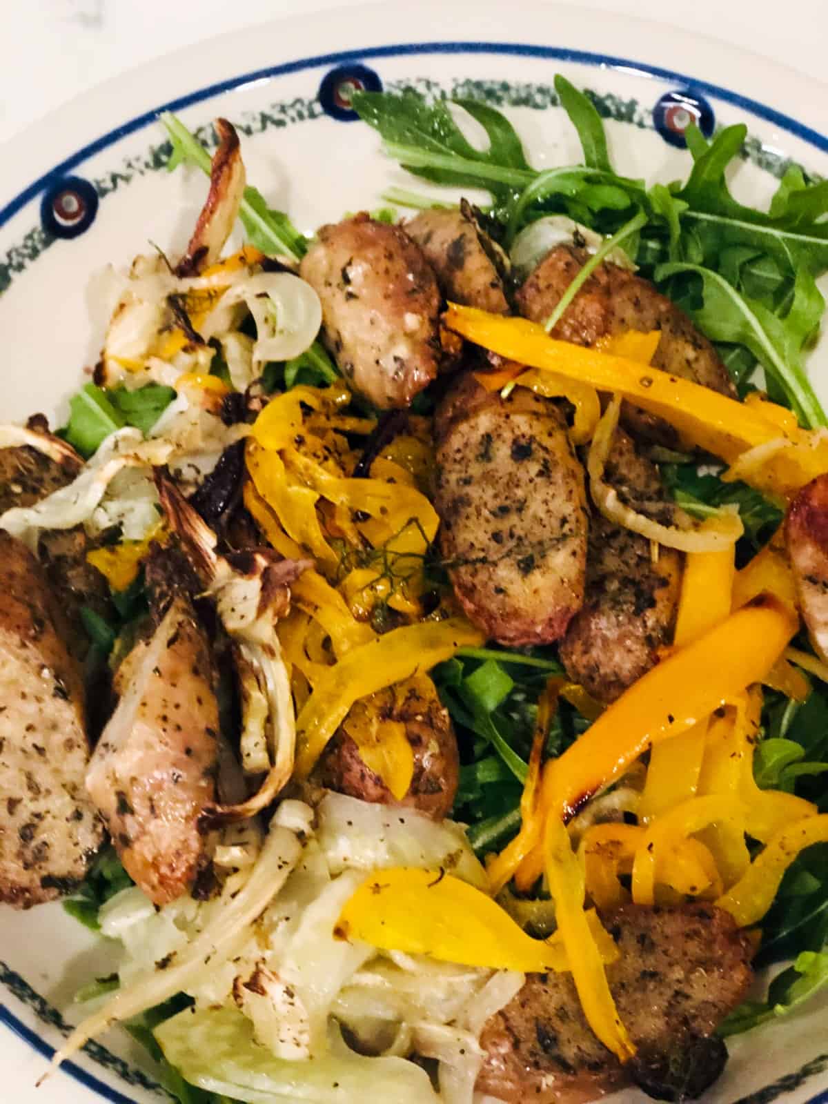 Fennel, sausage and peppers on arugula in white bowl.