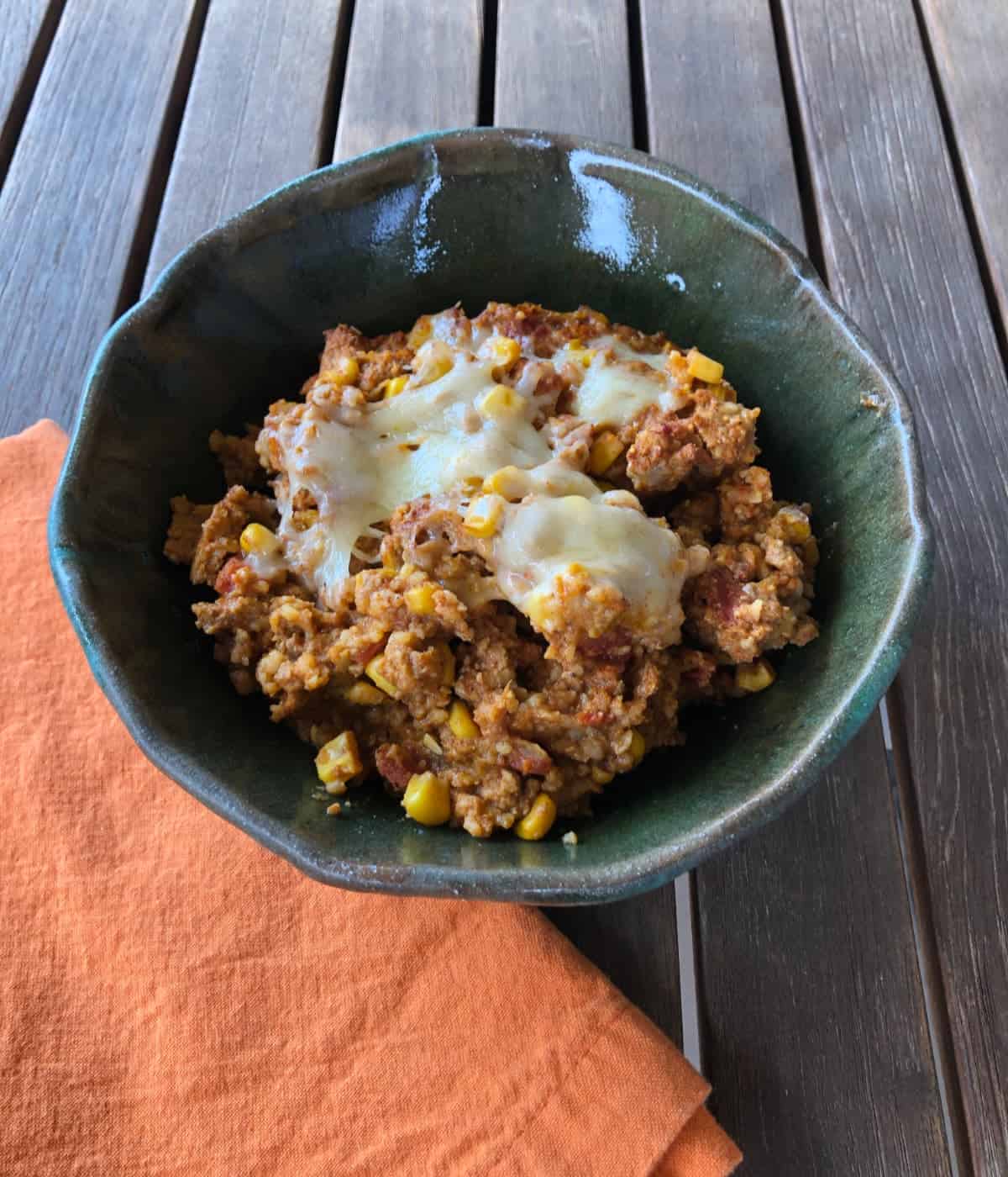 Slow cooker tamale pie in green ceramic bowl with orange napkin on wooden table.