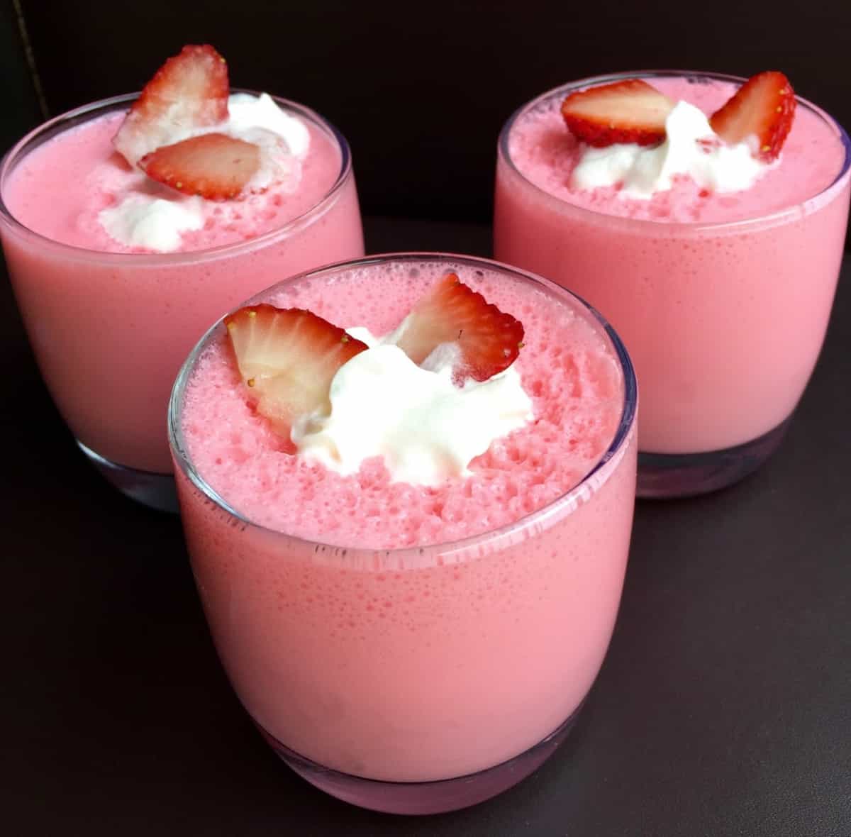 Three dessert glasses with strawberry jello yogurt fluff tipped with whipped creamed and sliced strawberries.