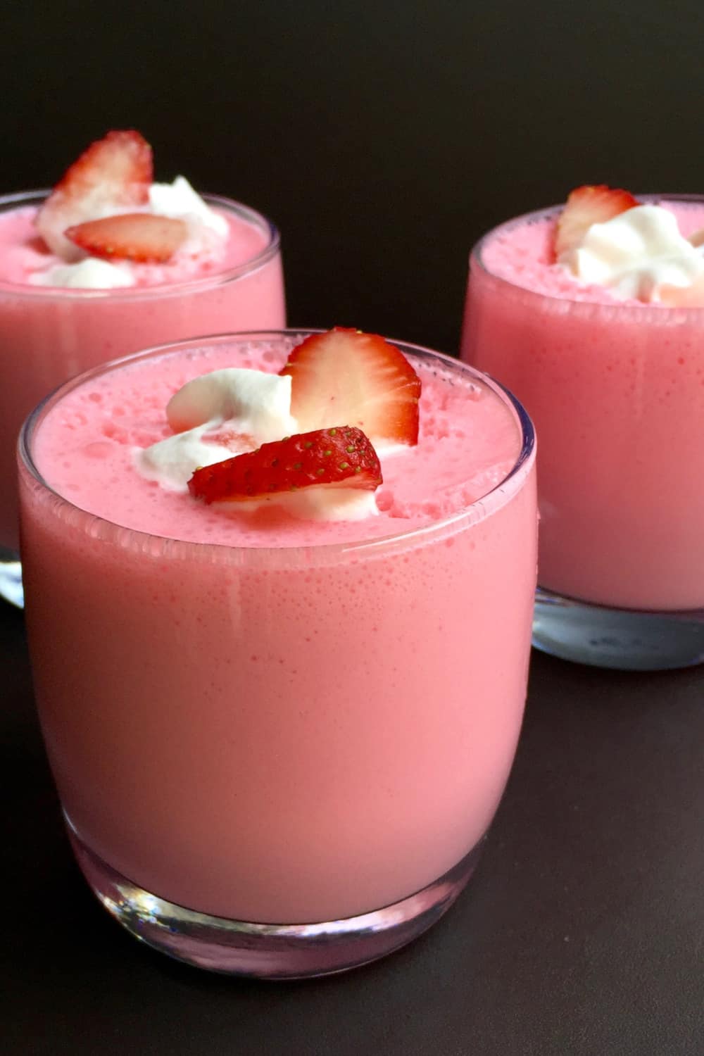 3 glasses of strawberry yogurt jello fluff topped with sliced strawberries.