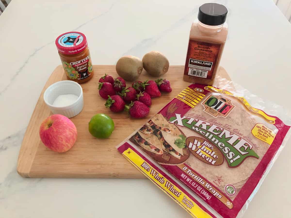 Ingredients for making fruit salsa including apple, lime, strawberries and kiwifruit on bamboo cutting board.