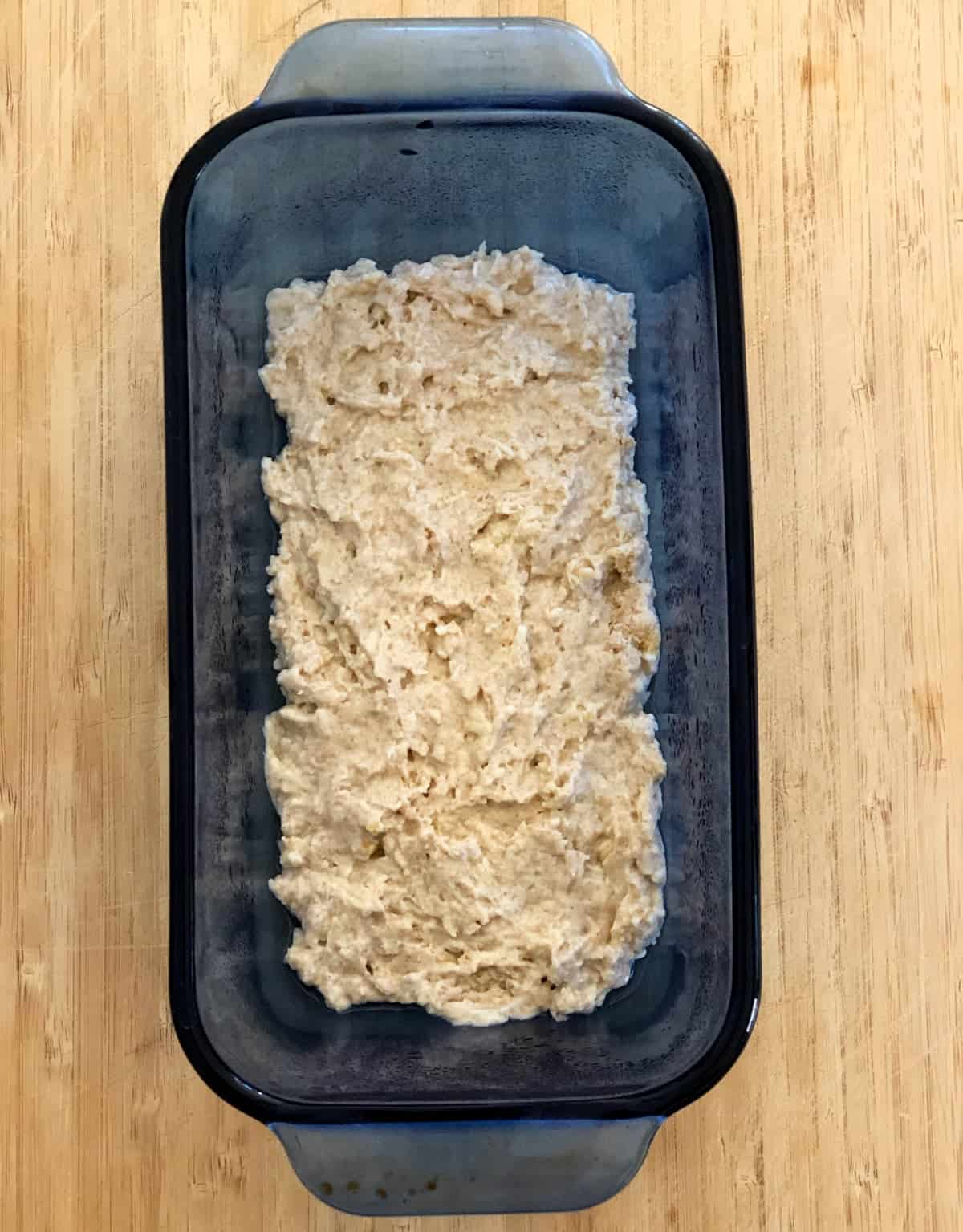 Prepared baking mix spread in blue glass loaf pan.