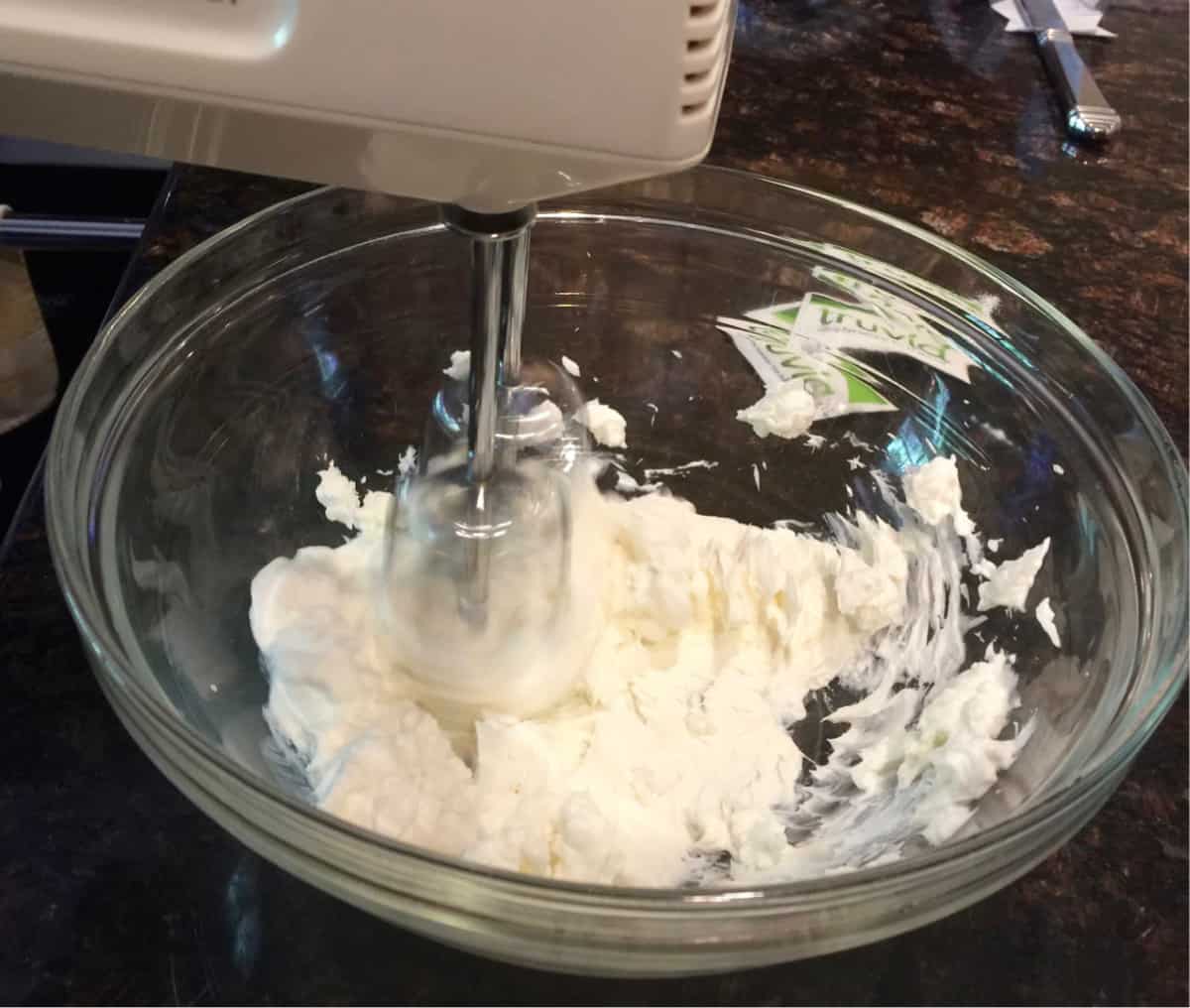 Beating cream cheese and sweetener in glass bowl with hand mixer.