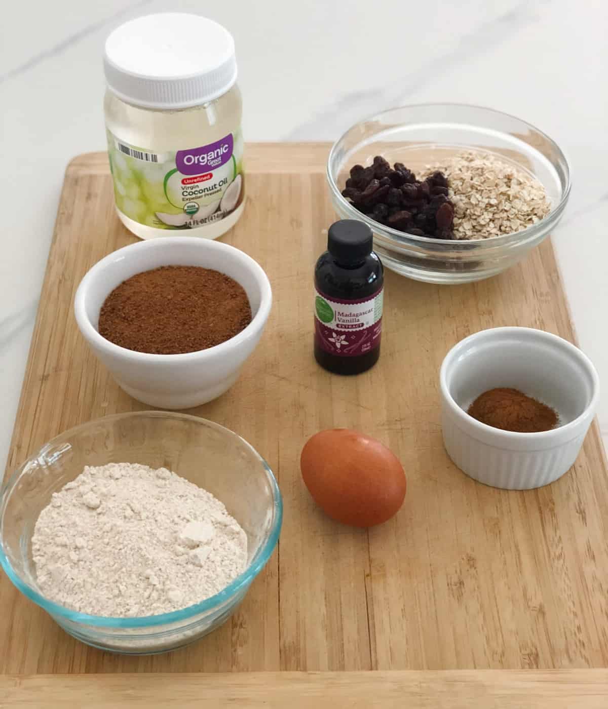 Coconut oil, sugar, flour, egg, vanilla, raisins, oats and cinnamon for making oatmeal raisin cookie.
