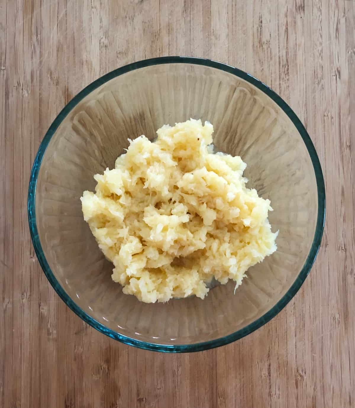 Glass mixing bowl with crushed pineapple on bamboo