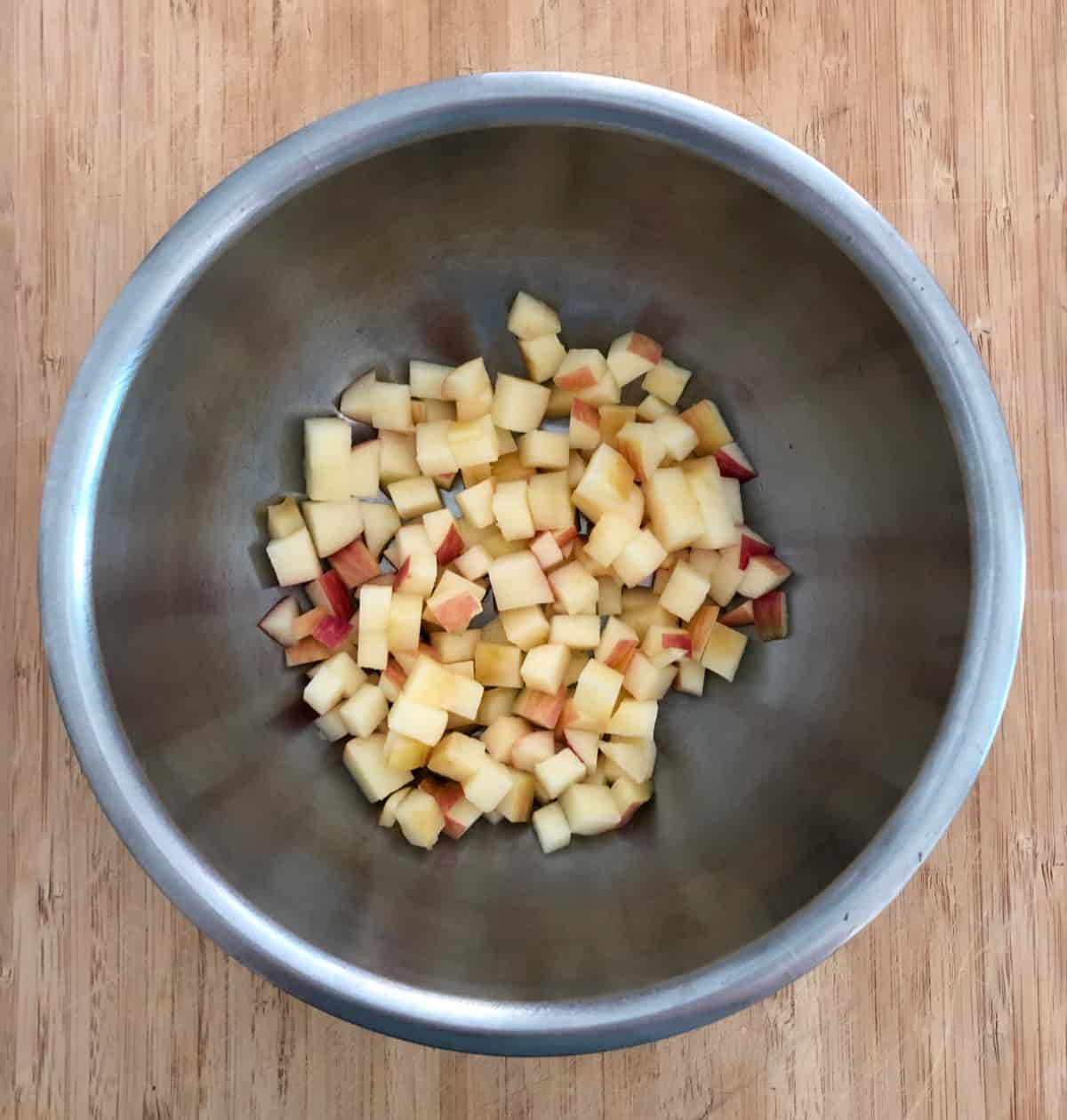 Diced apple tossed with lime juice in stainless mixing bowl on bamboo cutting board.
