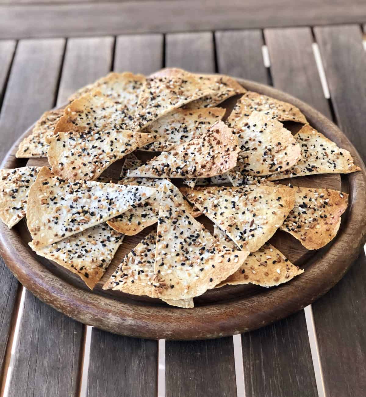 Everything but the bagel seasoned tortilla chips on wood serving platter on wooden table.