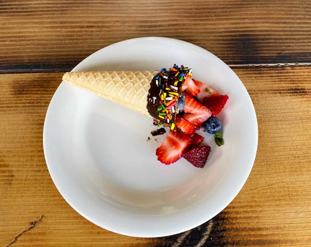 Chocolate dipped ice cream cone filled with fresh berries on white plate.