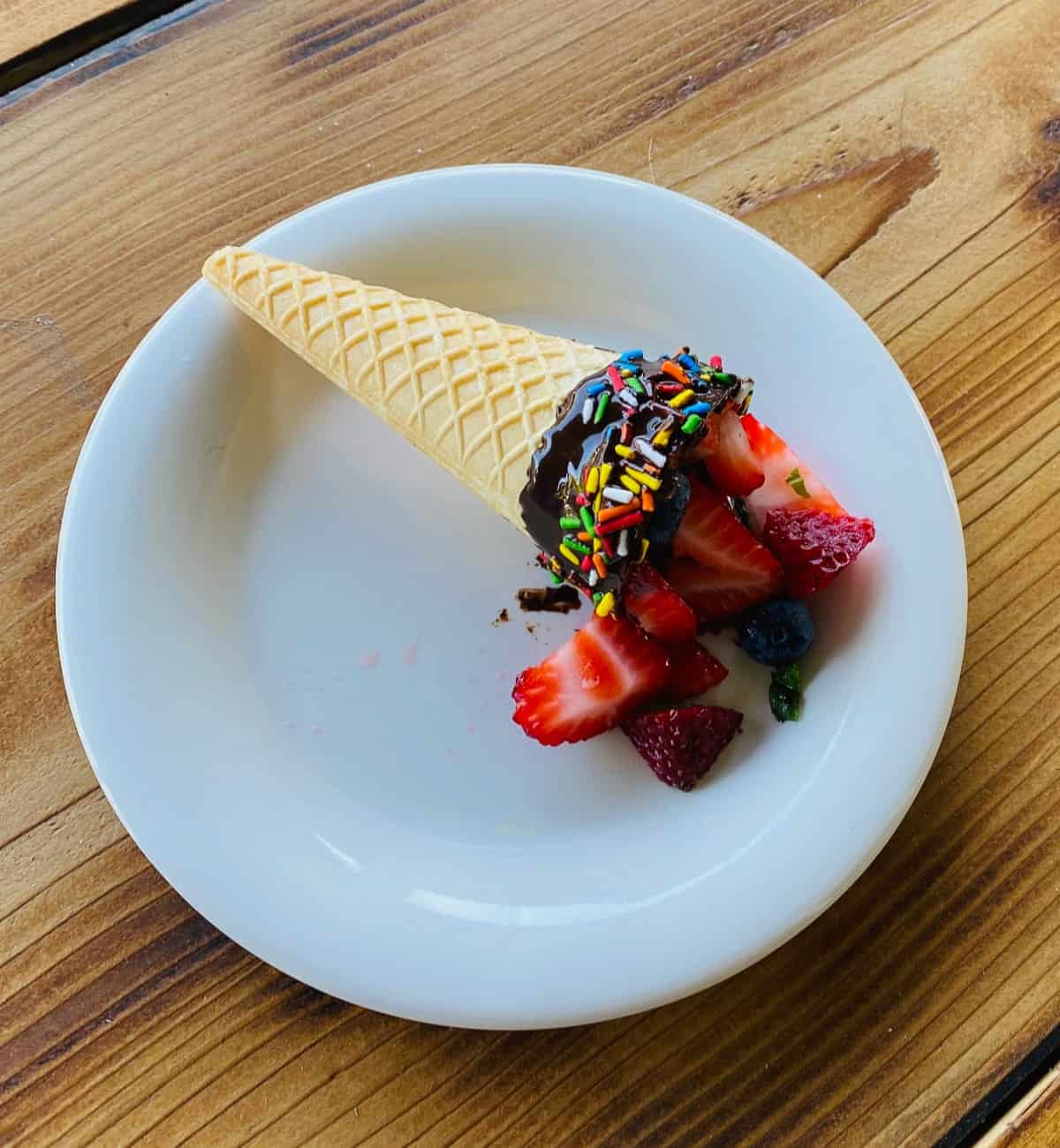 Fruit filled chocolate dipped cone in white plate on wood table.