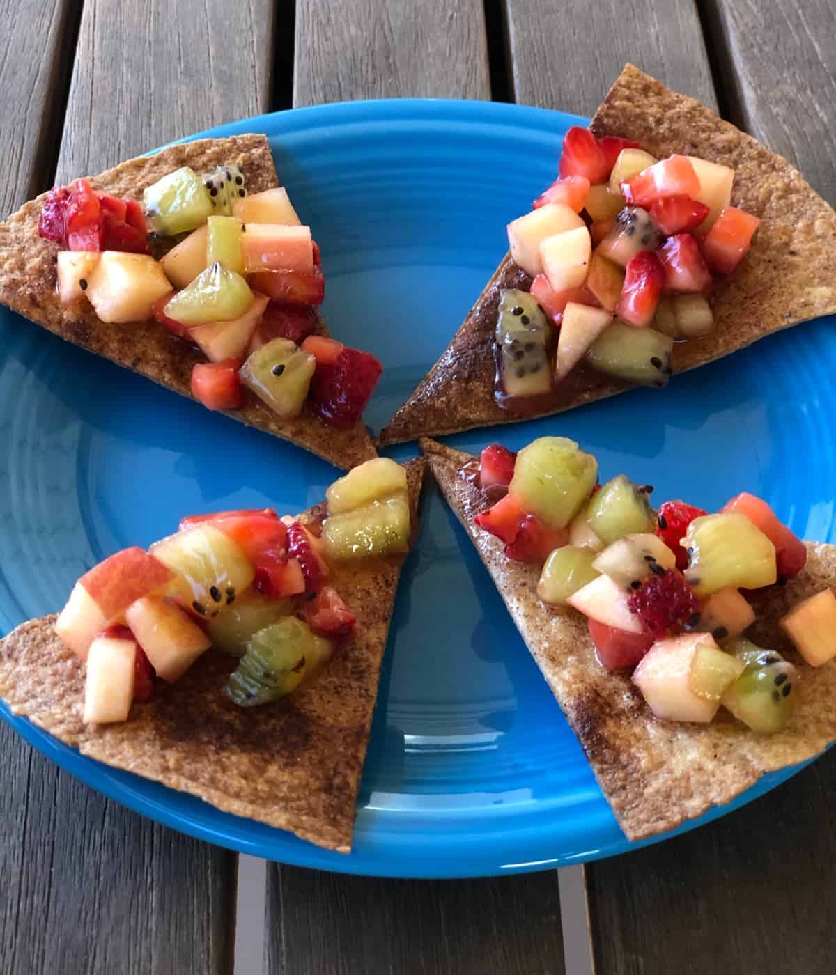 Four cinnamon-sugar crisps topped with fruit salsa on blue plate.
